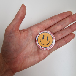 Bedž sa žutim smiley dizajnom i natpisom You Deserve Happiness, prikazan u ruci.