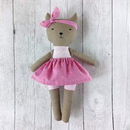 Šivena igračka maca u roza suknjici i s roza mašnom na glavi na svetloj pozadini