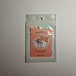 Magnet u obliku hrčka koji jede nudle iz kutije, spakovan u providnu kesicu sa holografskim ivicama.
