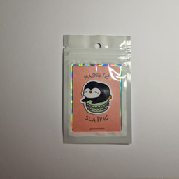 Magnet sa ilustracijom pingvina koji sedi na zelenom makaronu, spakovan u providnu kesicu sa holografskim ivicama.