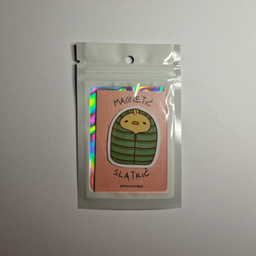 Magnet sa ilustracijom malog žutog pileta umotanog u zelenu vreću za spavanje, spakovan u providnu kesicu sa holografski