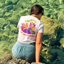 Žena nosi pamučnu, unisex, majicu sa ilustracijom korala i tekstom: THRIVING IN WARM SEAS.